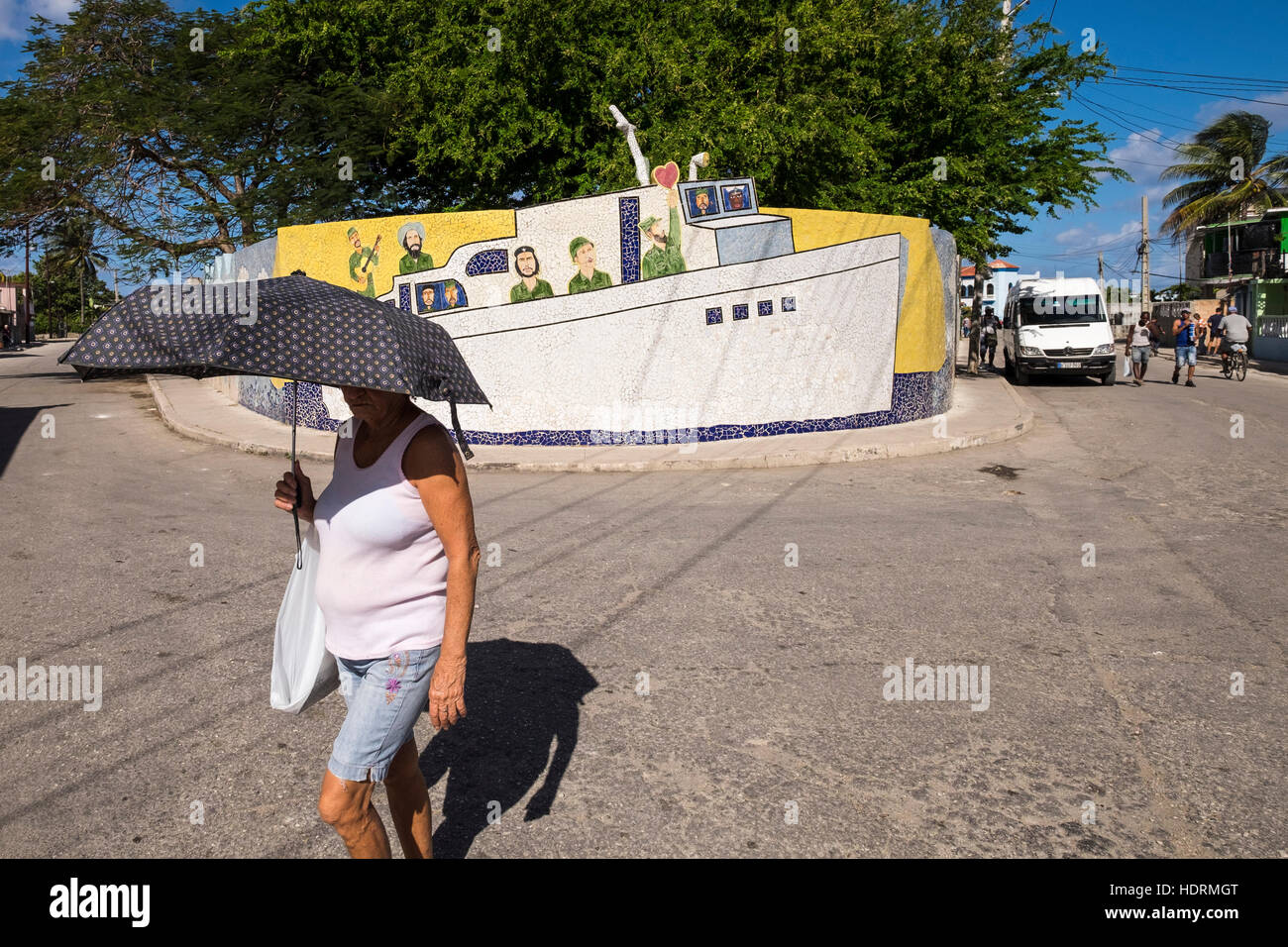 Woman with umbrella walks past tiled wall depicting the boat Granma with Che Guavara, Fidel Castro and others, Fusterland, La Havana, Cuba. Stock Photo