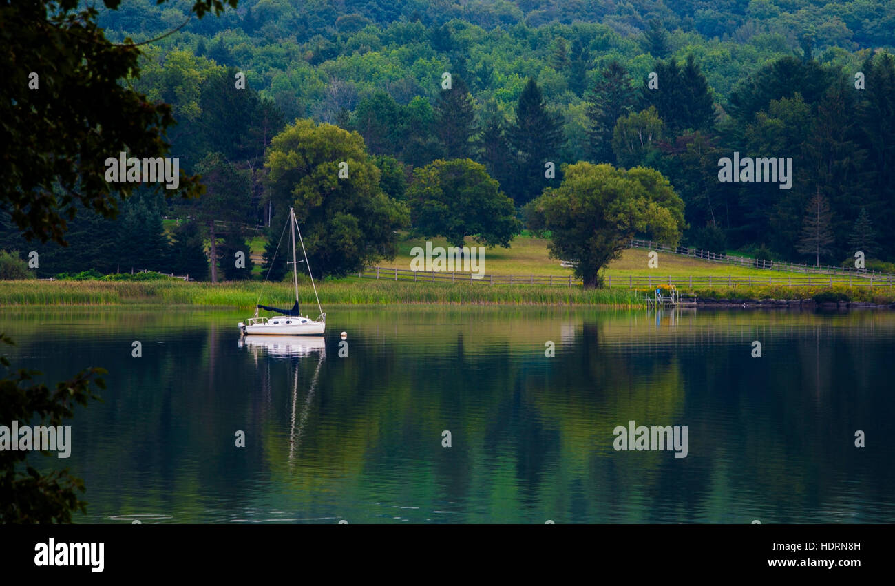 Sailboat at dusk on a lake with the mirror image reflected in the water; Knowlton, Quebec, Canada Stock Photo