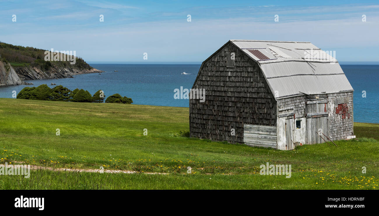 A worn wooden building on a grass hillside overlooking the ocean; Saint