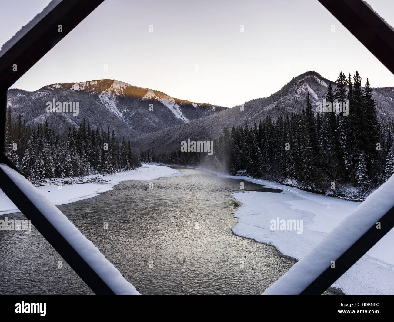 A landscape with snow along the shoreline of a lake and a mountain range viewed through a diamond shaped window frame; British Columbia, Canada Stock Photo