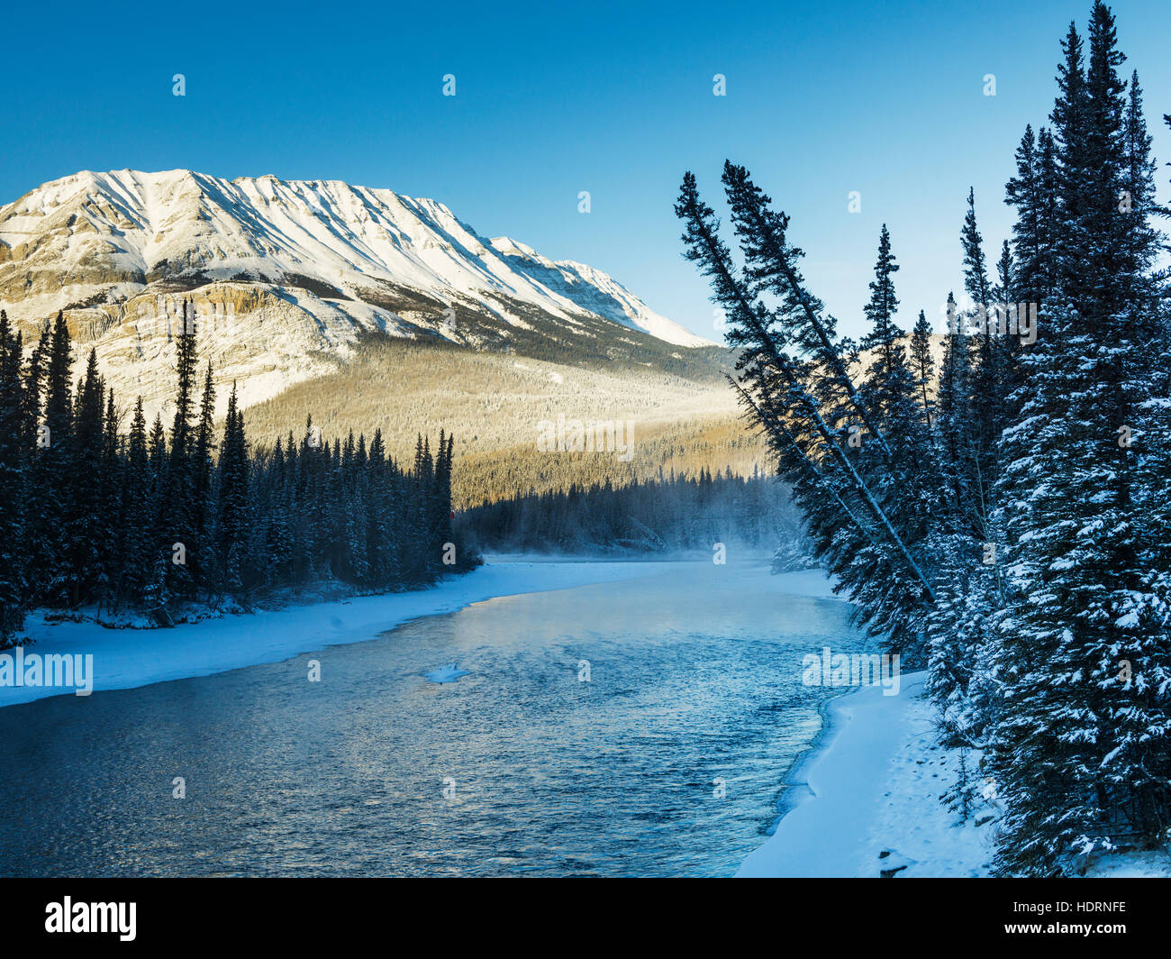 A landscape with snow along the shoreline of a lake and a snow covered mountain; British Columbia, Canada Stock Photo