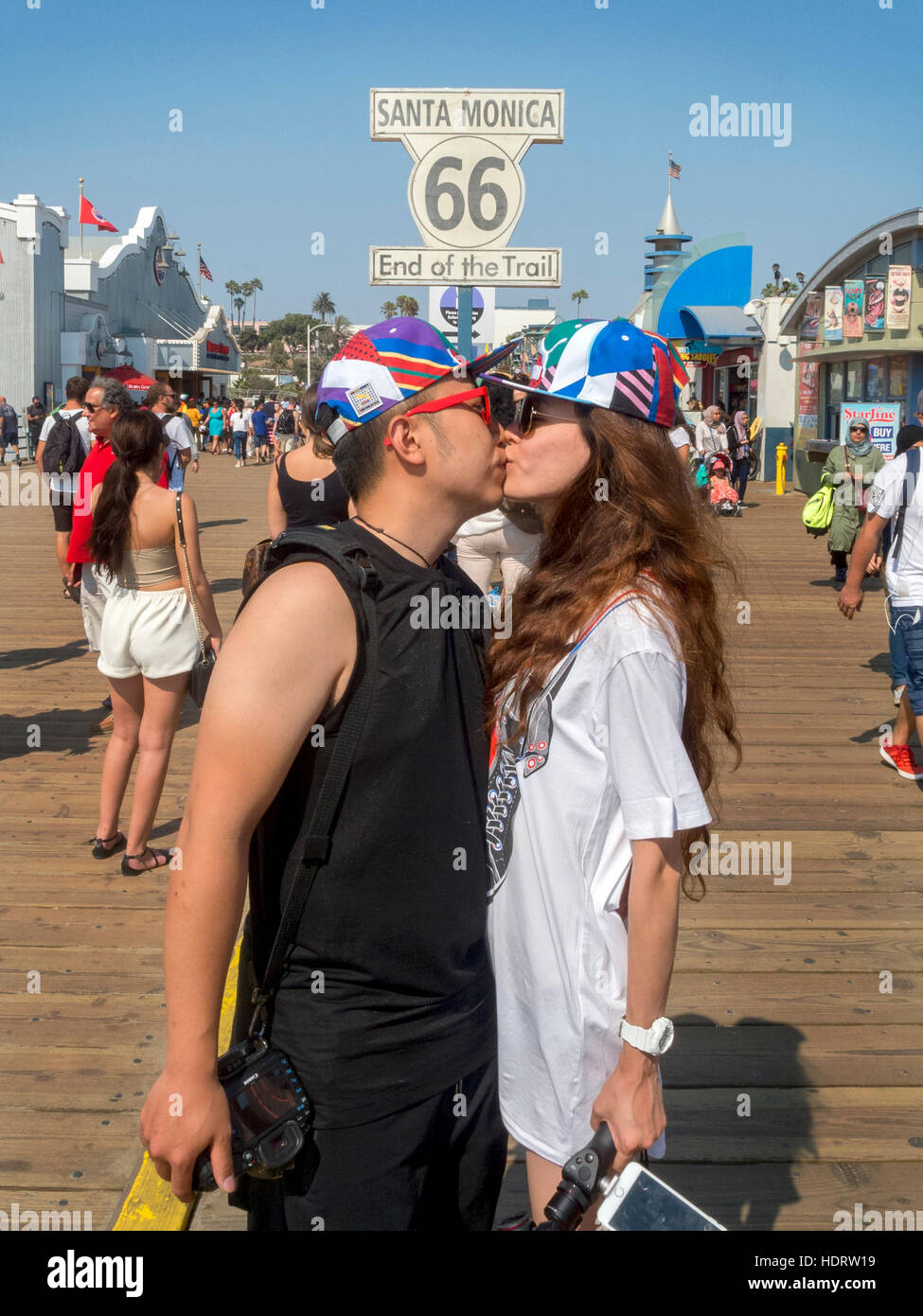 An Asian American couple kiss on the amusement pier in Santa Monica, CA, at the western end of US Route 66 highway. Note sign. Stock Photo