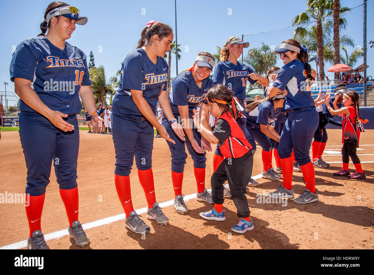Multiracial college women's softball players trade hand slaps with a little girl admirer as they prepare for a game on the field in Fullerton, CA. Stock Photo