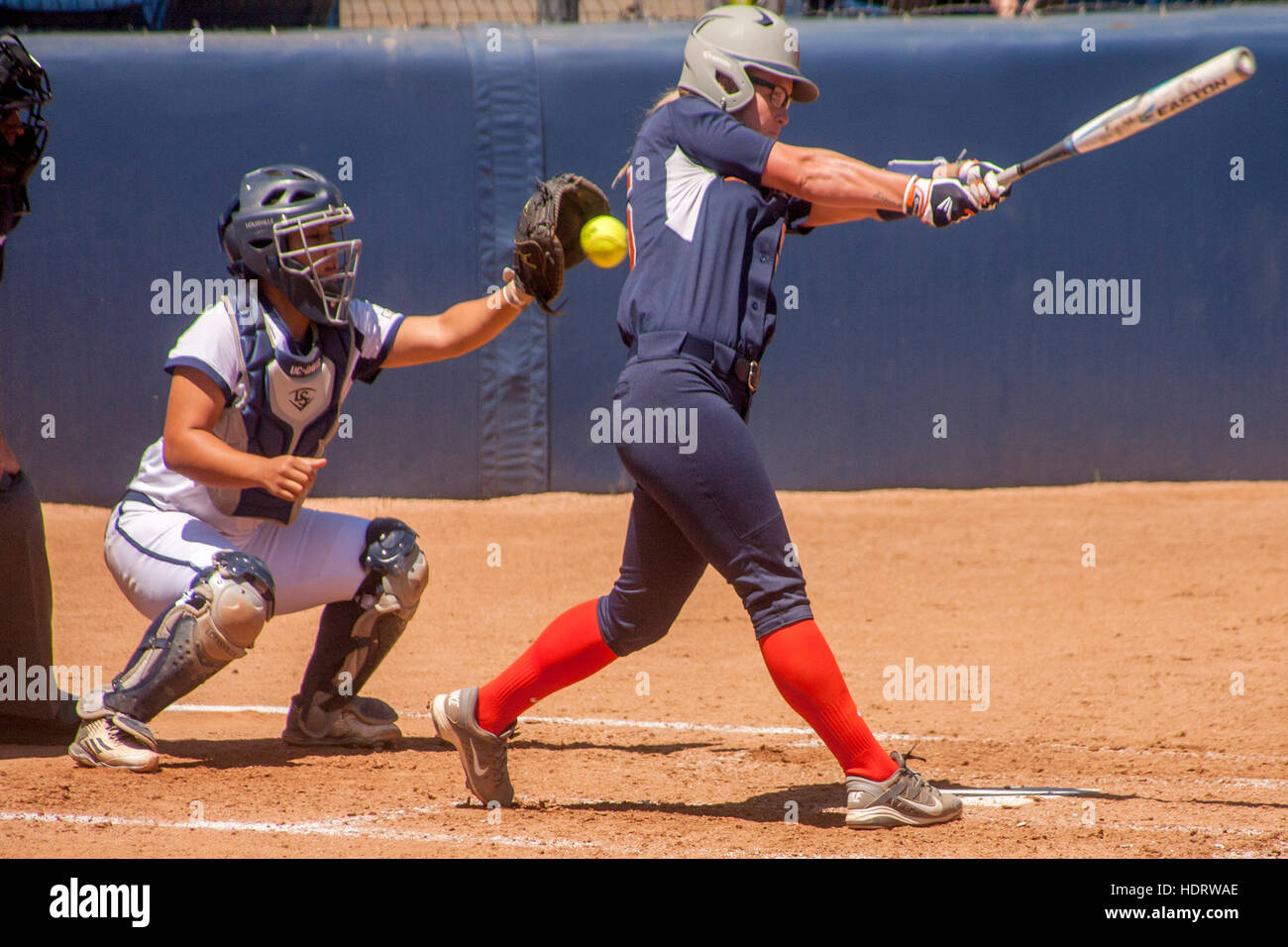 Up at bat, a college woman softball player swings at the ball and