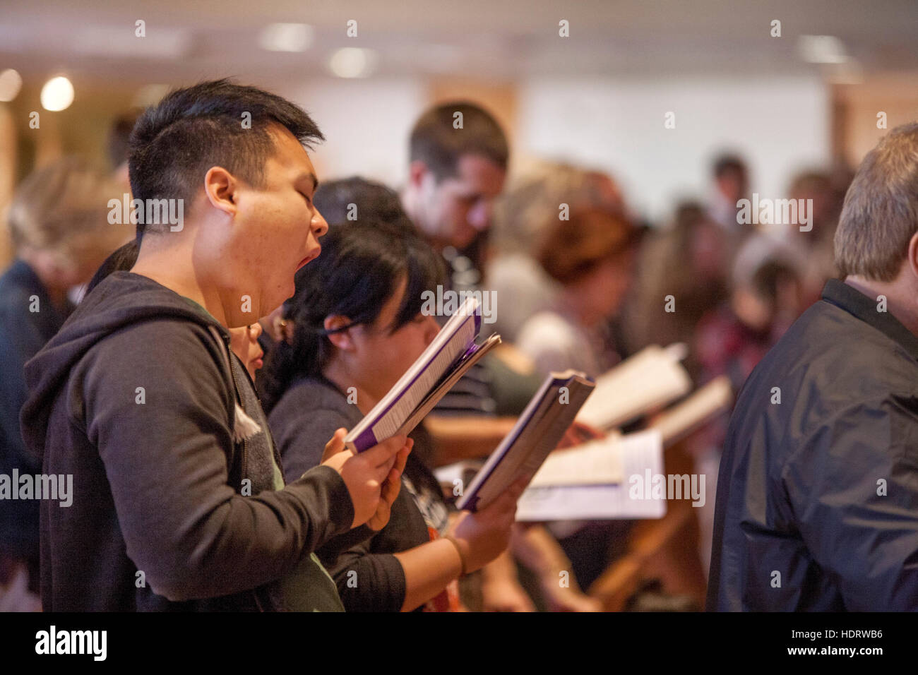An Asian American parishioner yawns while singing a hymn during mass at a Laguna Niguel, CA, Catholic church. Stock Photo