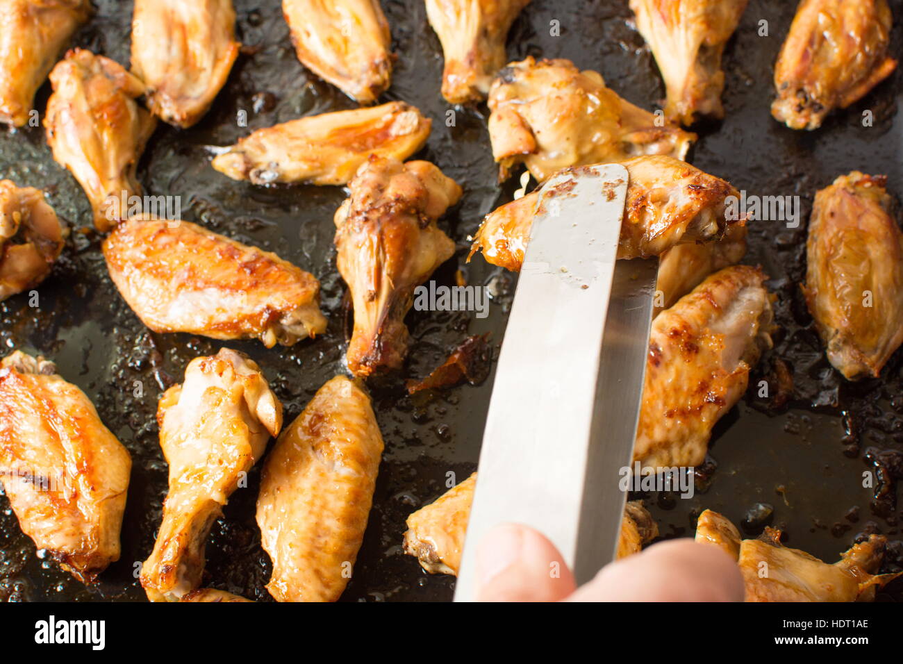 Cooking tongs holding bbq chicken wings on black plate Stock Photo Alamy