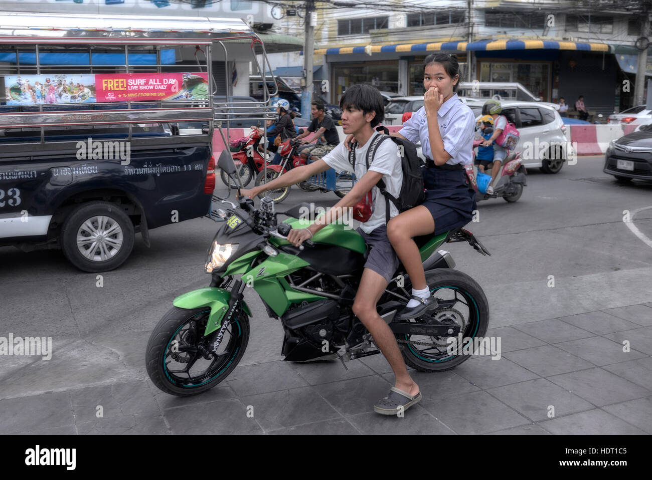 Motorbike young rider. Thailand street scene with older brother collecting younger sister from school on his motorbike. Neither wearing safety helmet. Stock Photo