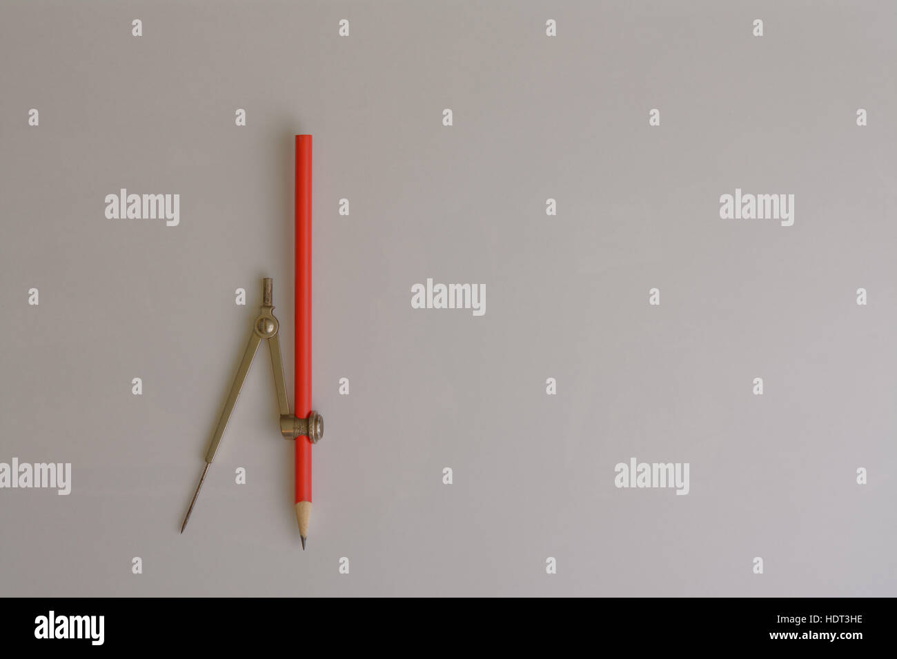A standard drawing compass fitted with a red pencil on a blank background. Stock Photo