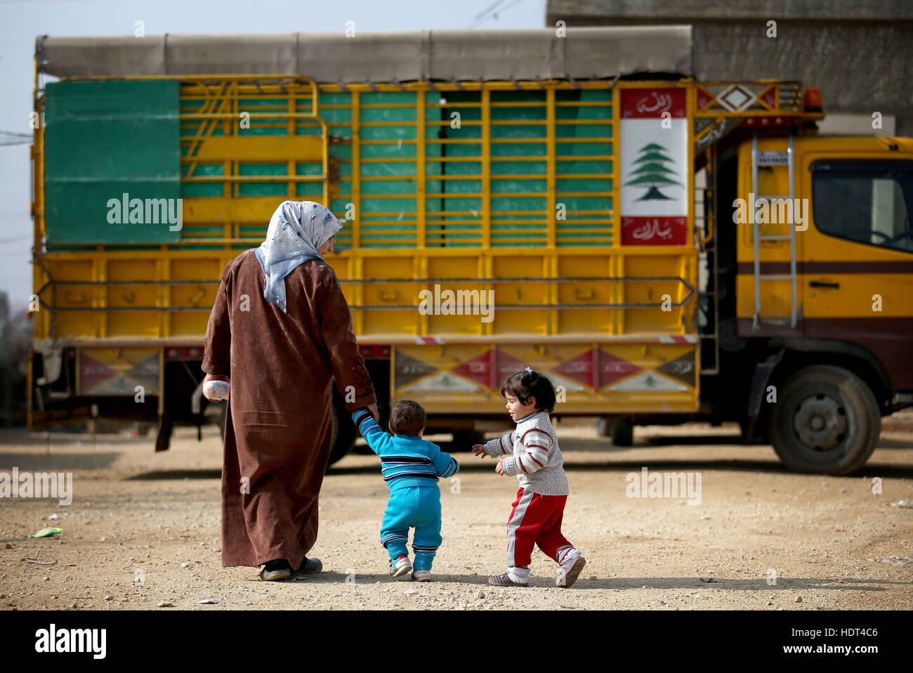 A Syrian refugee woman and her children walk back to their tent after visiting the doctor in a refugee camp near Taalabaya in the Bekaa Valley. Stock Photo
