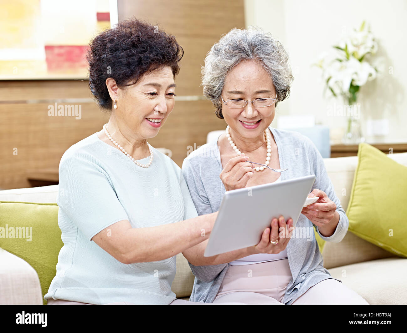 two senior asian women sitting on couch using tablet computer, happy and smiling Stock Photo