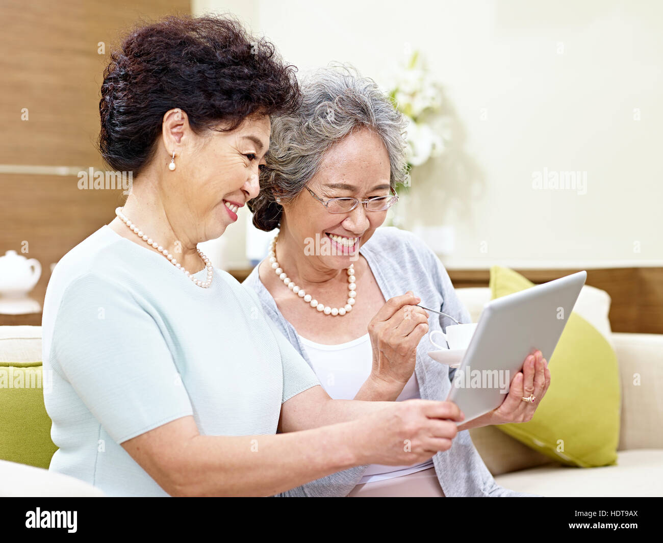 side view of two senior asian women sitting on couch taking a selfie using mobile phone, happy and smiling Stock Photo
