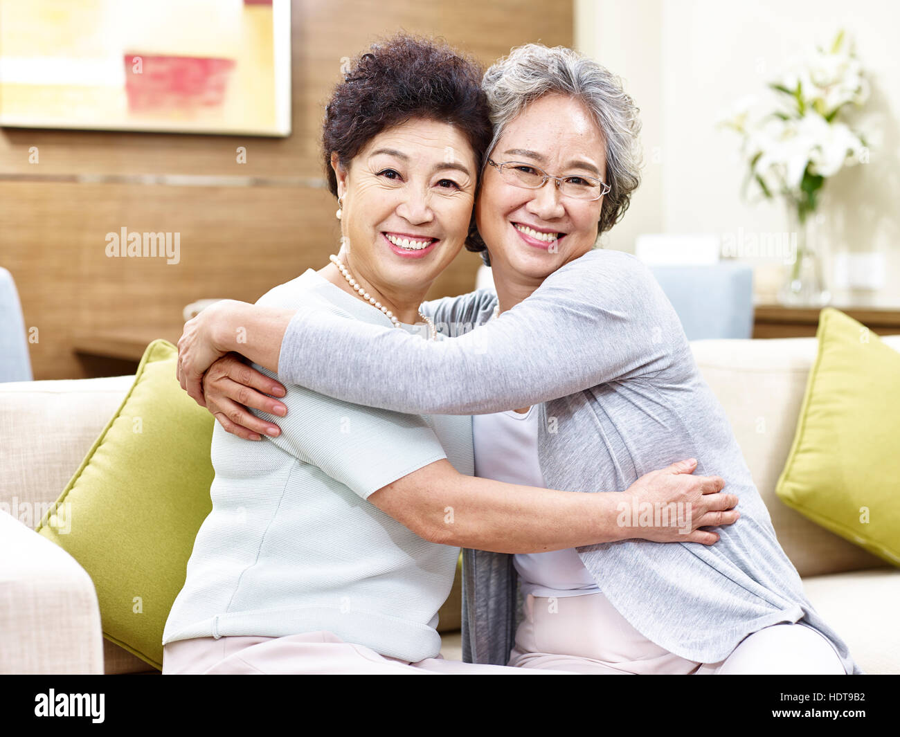 two senior asian women sitting on couch hugging each other, happy and smiling Stock Photo