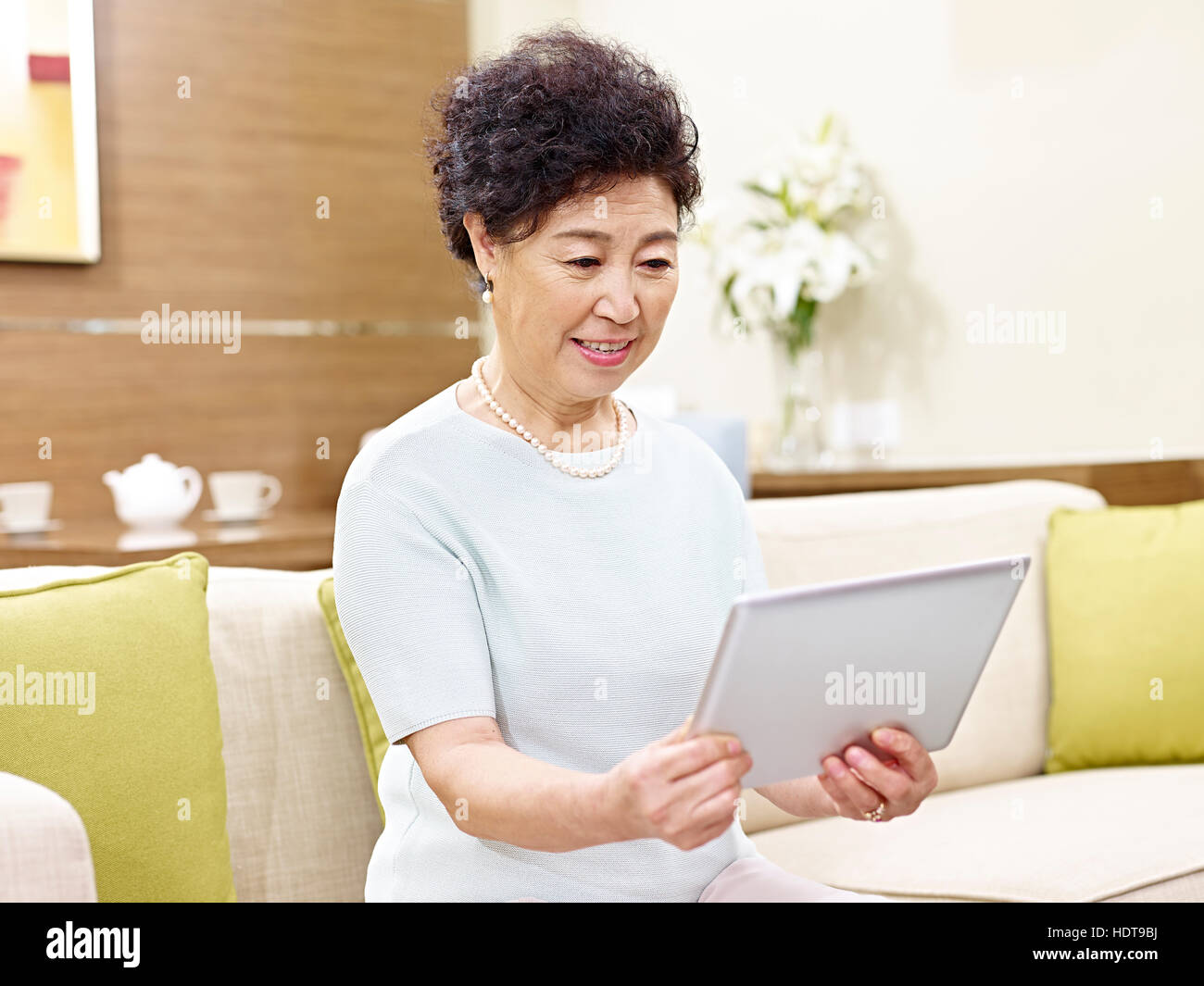 senior asian woman sitting on couch looking at tablet computer Stock Photo