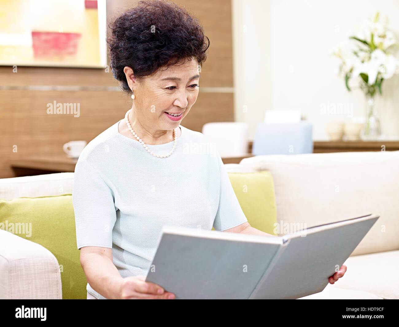 senior asian woman sitting on couch reading a book Stock Photo