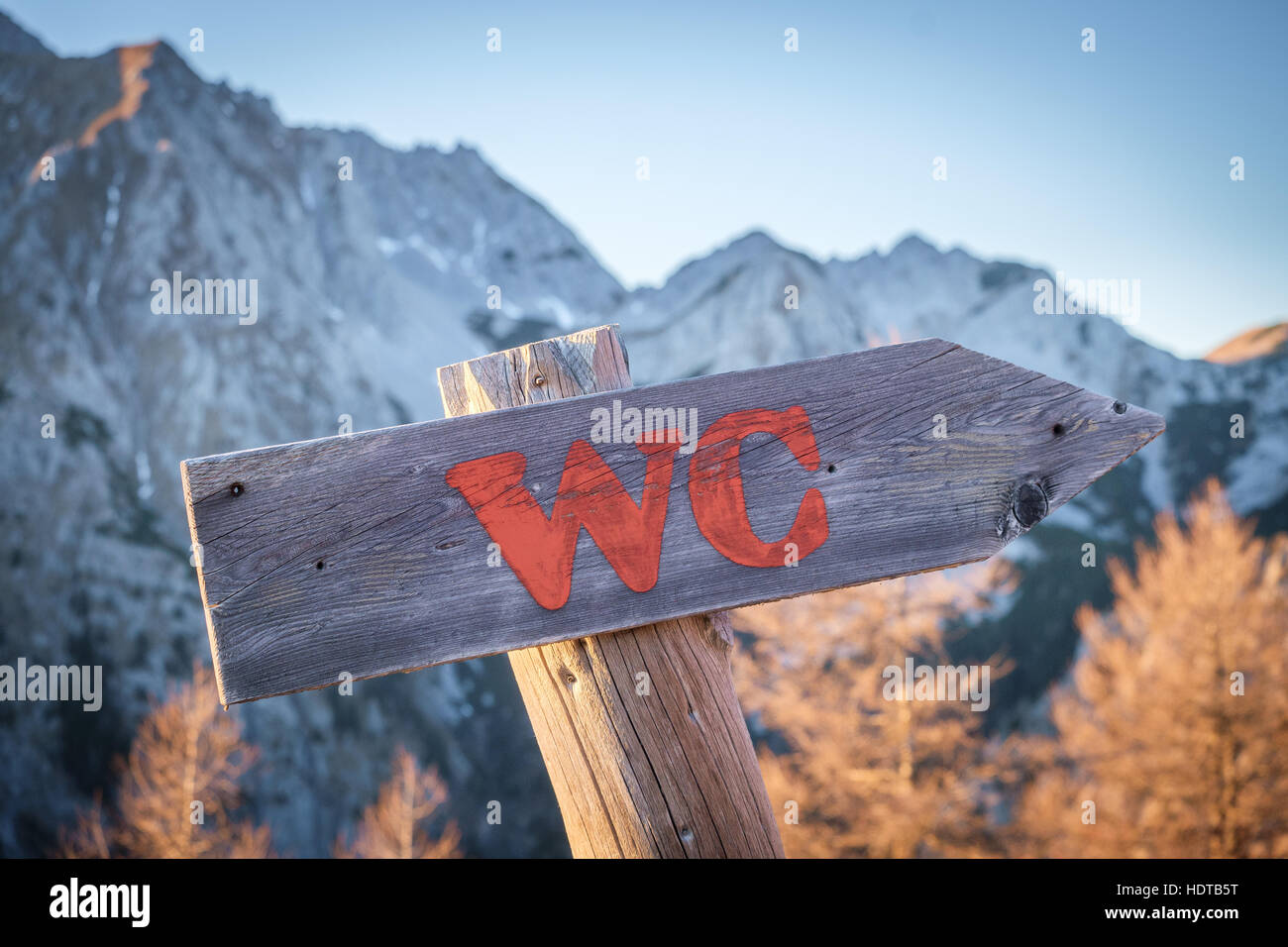 Arrow board pointing towards toilet near a mountain hut. Mountains in the background. Stock Photo