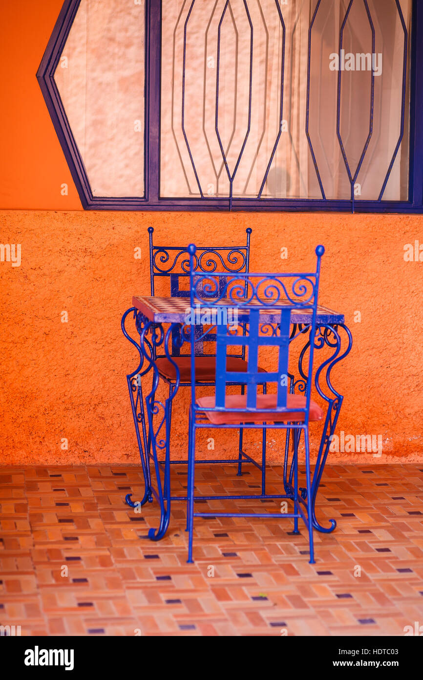 Two blue chairs and a blue table in front of orange painted wall Stock Photo