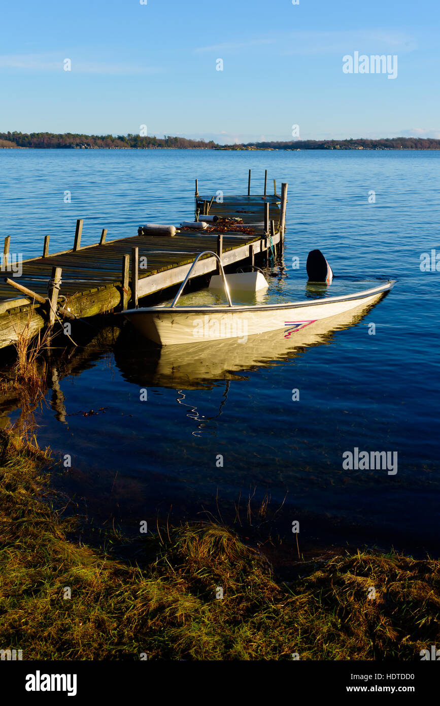 Sunken motorboat moored at a wooden pier and abandoned. Sea is motionless and calm. Stock Photo
