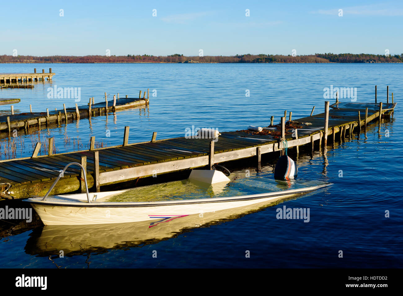 Sunken motorboat moored at a wooden pier and abandoned. Sea is motionless and calm. Stock Photo