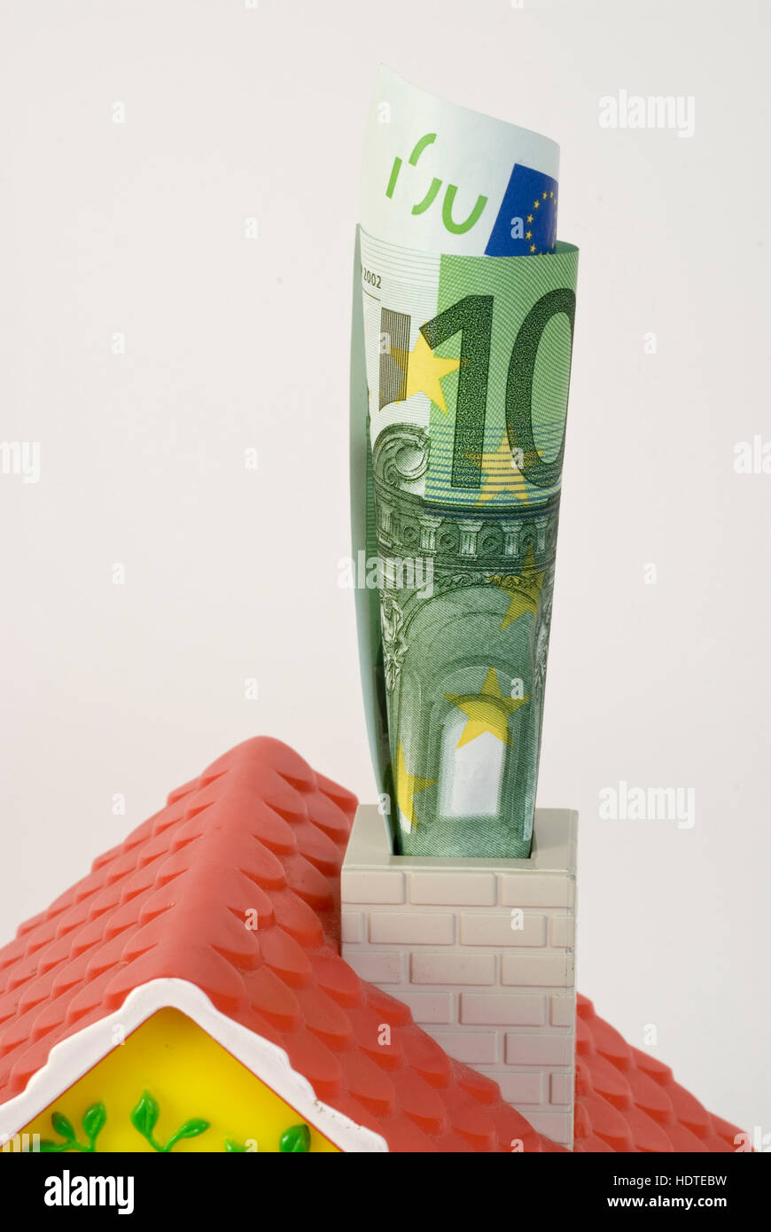 Miniature house with rolled-up banknote in the chimney, symbolic picture for saving energy Stock Photo