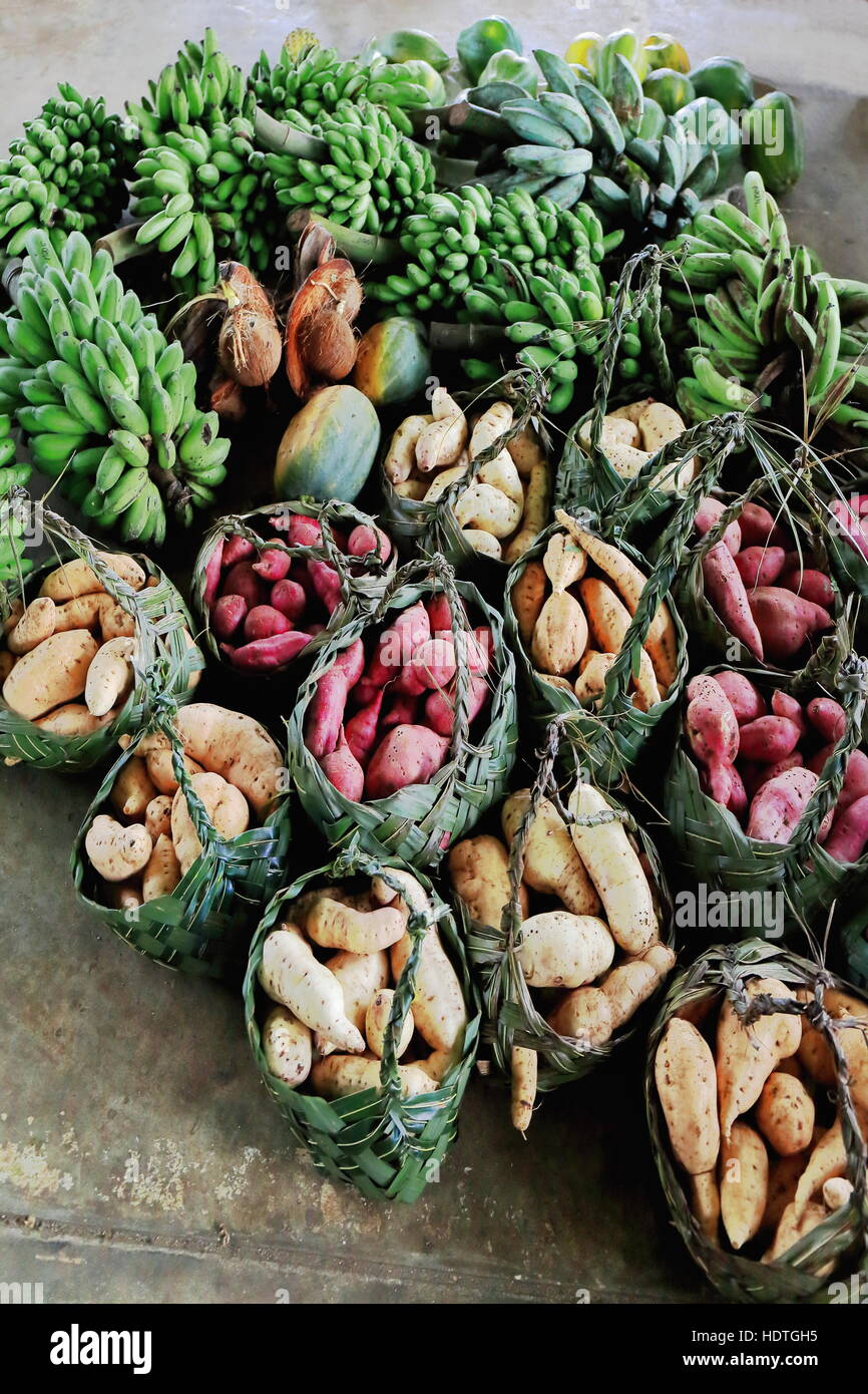 Vegetables and fruits -yam-sweet potato-papaya-coconut-banana-plantain- in coconut leaf baskets on concrete floor on sale at the main market of Luganv Stock Photo