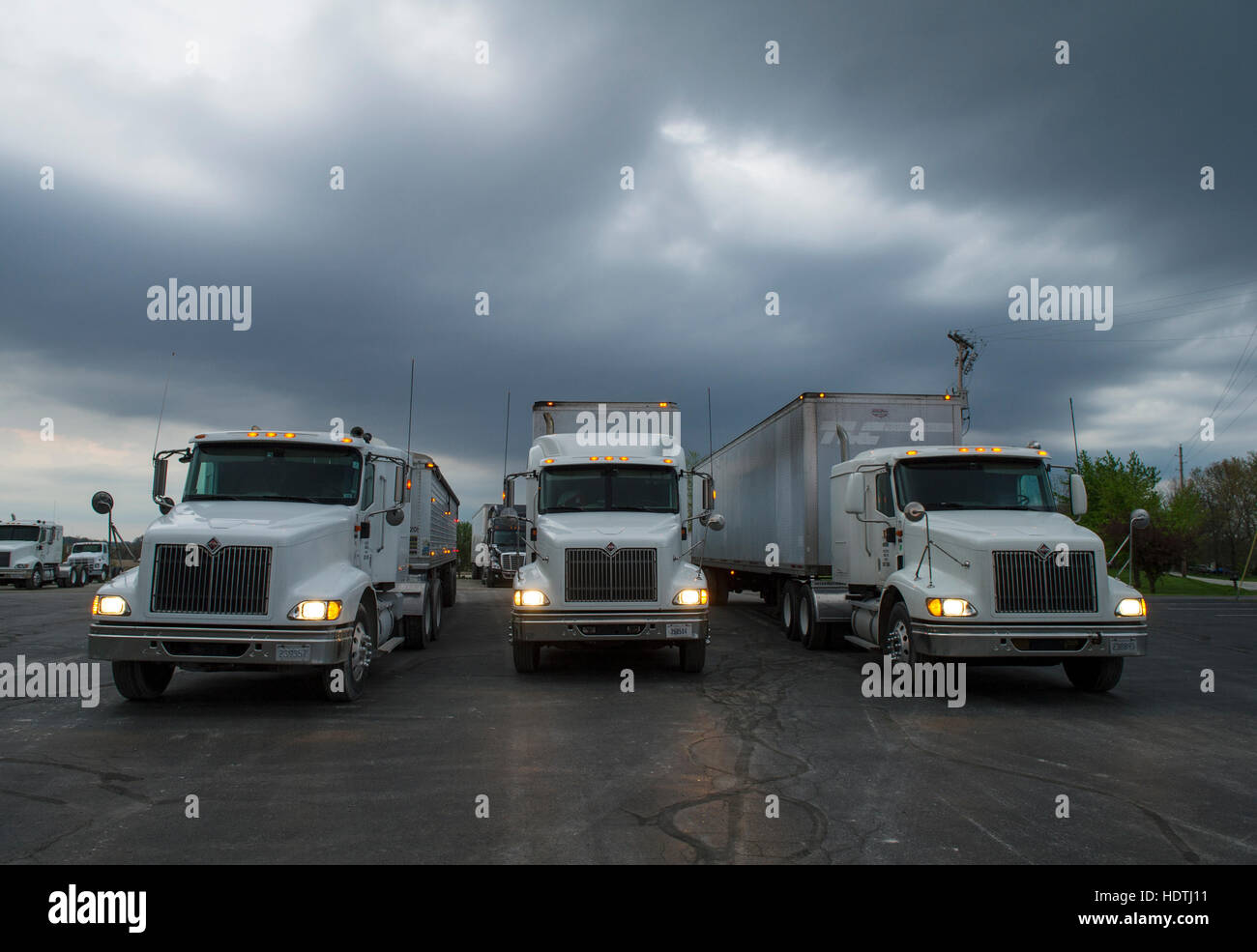 Three semi tractor-trailer trucks idling in a parking lot on a storm threatening evening. Stock Photo