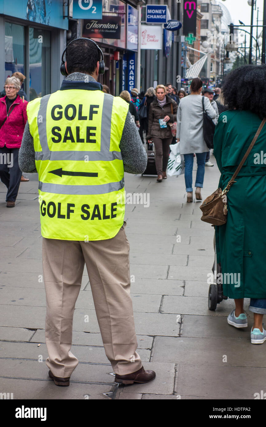 Shoppers passing man wearing high visibility jacket with Golf Sale advertising sign. Oxford Street, London Stock Photo