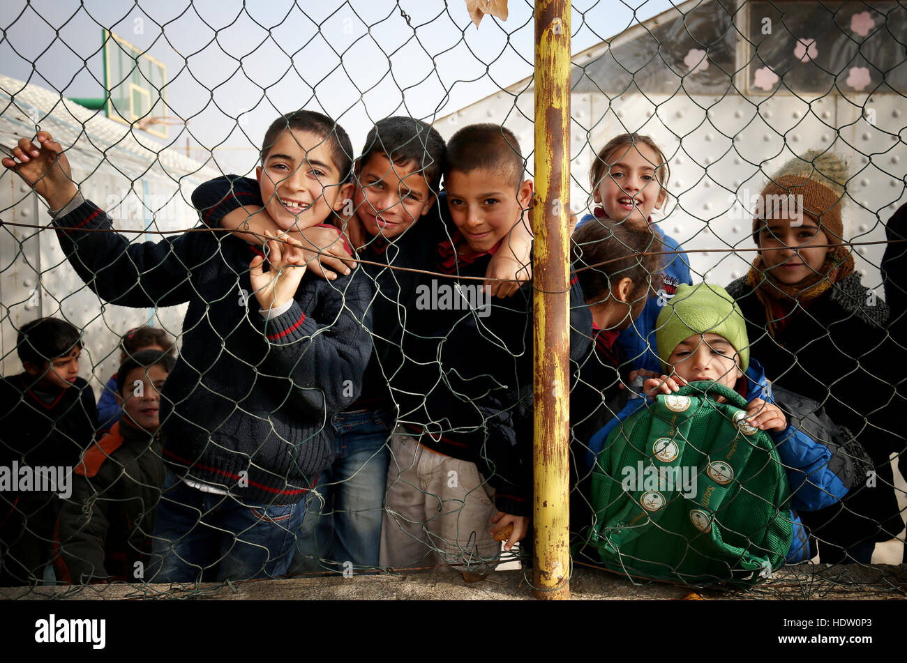 Syrian refugee children peep through the perimeter fence of an old former basketball court that is now their school playground in a refugee camp near Taalabaya in the Bekaa Valley. Stock Photo