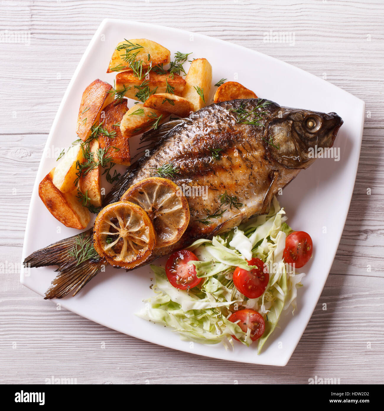 grilled fish with fried potatoes and salad on a plate. top view closeup