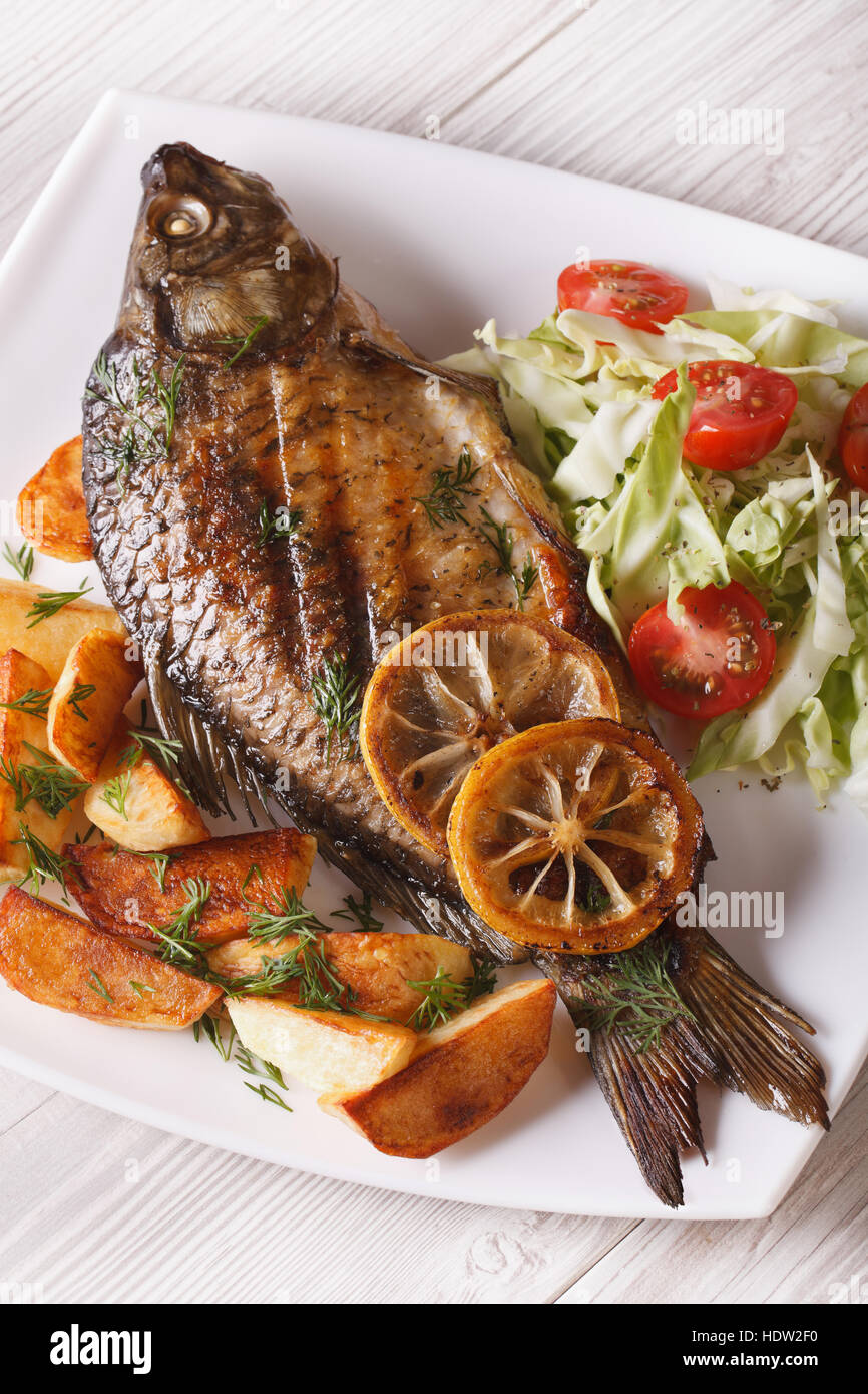 grilled fish carp with fried potatoes and salad on the plate closeup. vertical top view Stock Photo