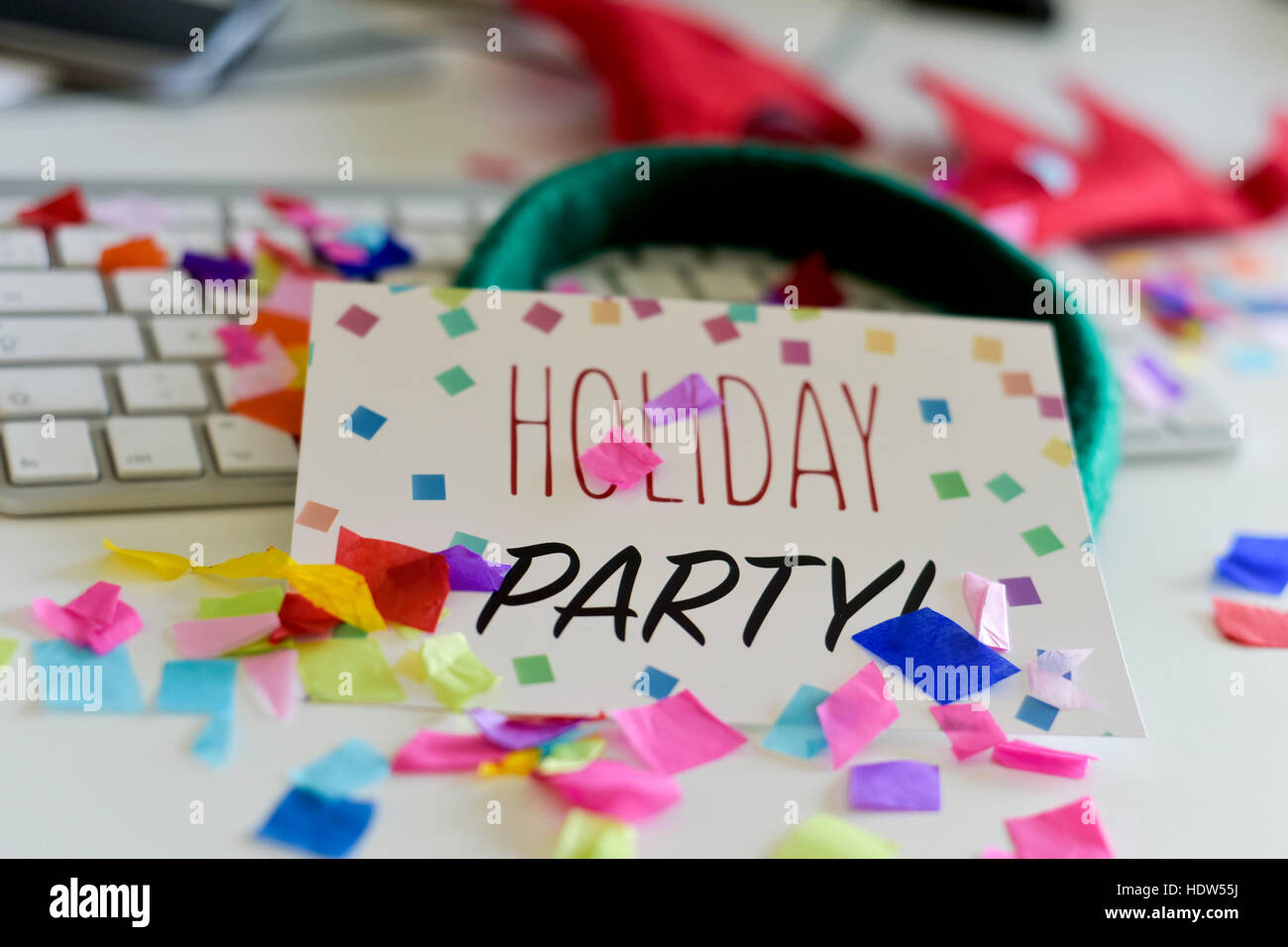 closeup of an office desk full of confetti with a signboard with the text holiday party in the foreground and a reindeer antlers headband on a compute Stock Photo