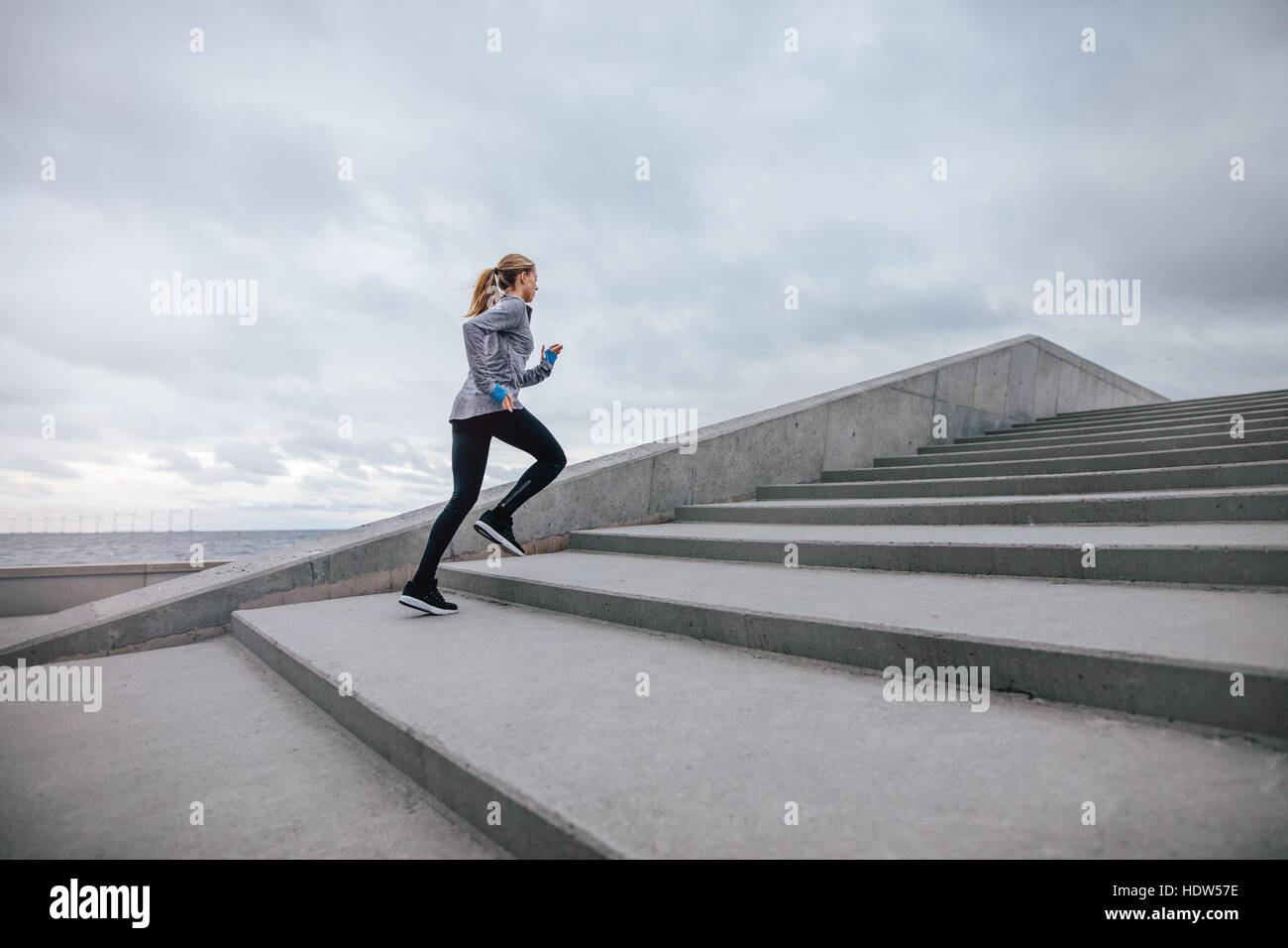 Full length shot of healthy woman climbing up on stairs. fitness female exercising outdoors in morning. Stock Photo