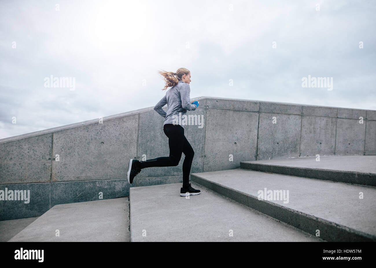 Side view full length shot of fit young woman running up stairs. Fitness female on morning workout. Stock Photo