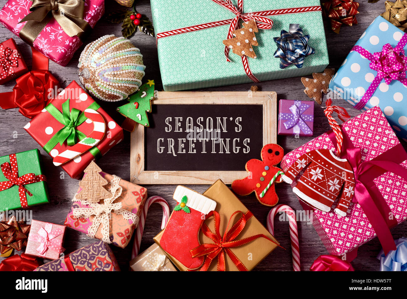 high-angle shot of some christmas ornaments, cookies, a pile of gifts tied with ribbons of different colors, and a chalkboard with the text seasons gr Stock Photo