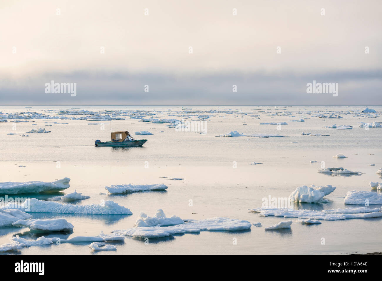 A small outboard boat motors through icebergs in the Arctic Ocean on a calm evening, North Slope