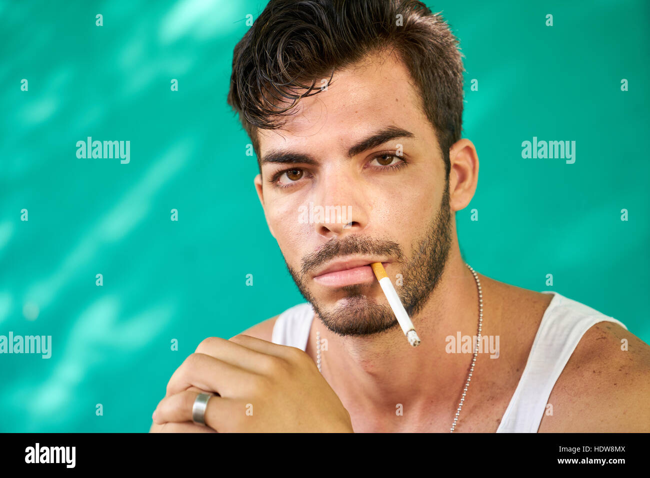 Real Cuban people and emotions, portrait of young hispanic man from Havana, Cuba looking at camera with serious expression, smoking cigarette and blow Stock Photo