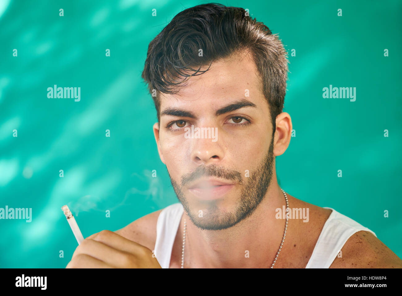 Real Cuban people and emotions, portrait of young hispanic man from Havana, Cuba looking at camera with serious expression, smoking cigarette and blow Stock Photo
