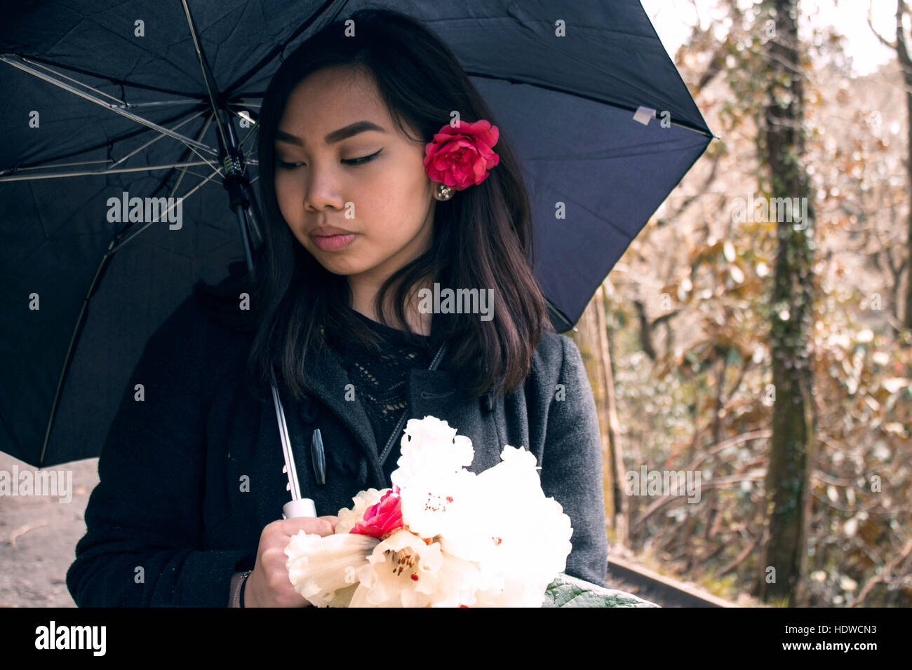 A young girl under an umbrella holding flowers Stock Photo