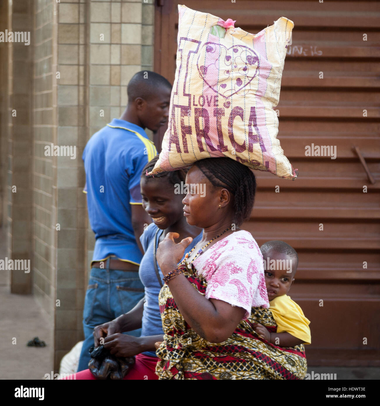 'I love Africa' - Woman carrying bag with inscription on her head and baby on her back. Optimism and joie de vivre reign in Sierra Leone Stock Photo