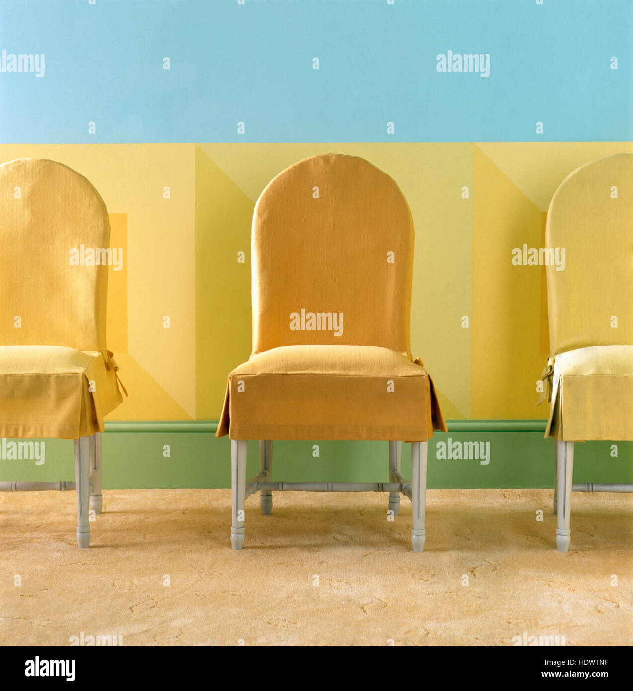 Yellow loose covers on chairs against a yellow and turquoise painted wall Stock Photo