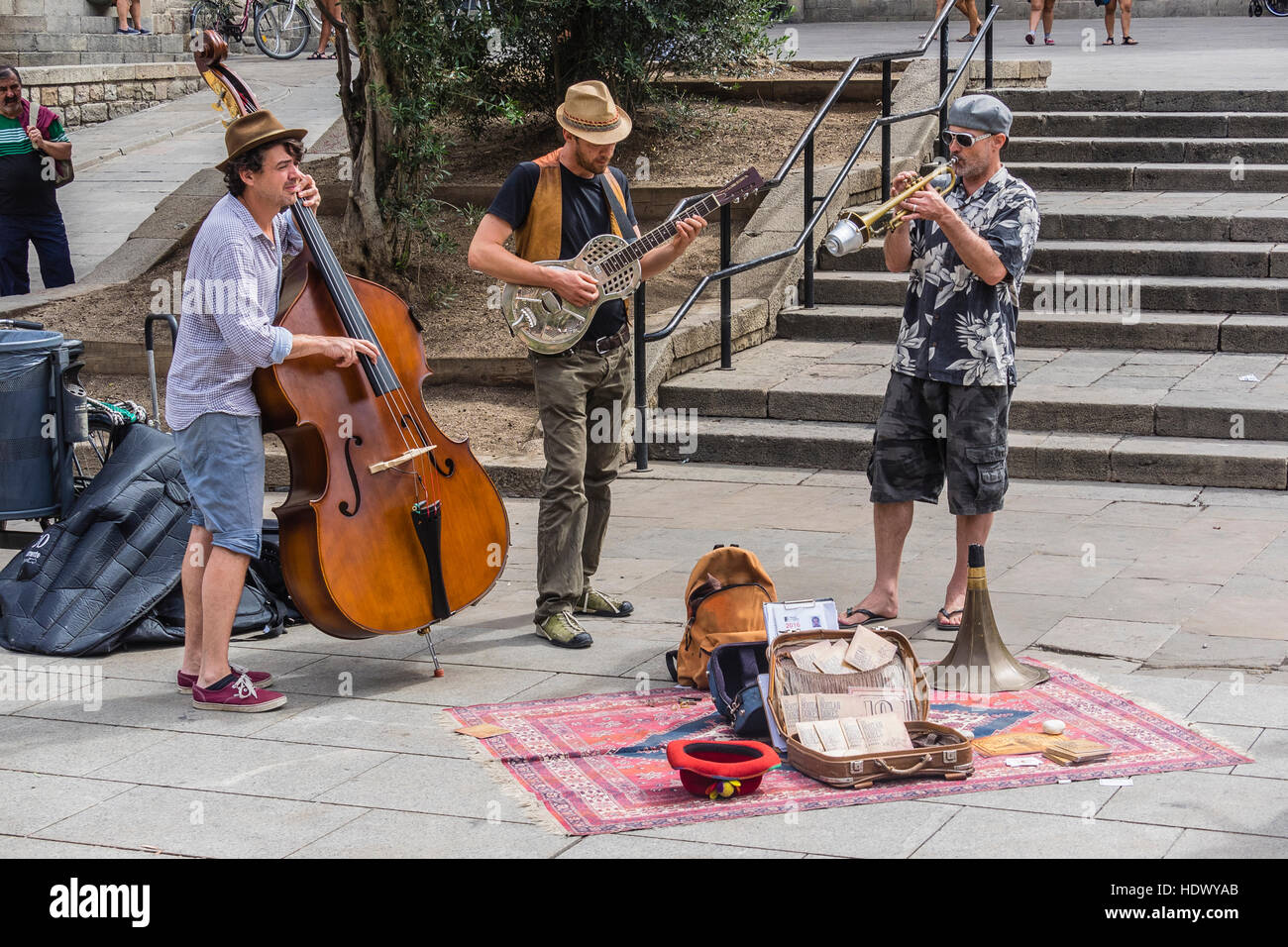 A trio of street musicians perform for the public in a plaza in Barcelona, Spain. They include a bass player, a guitarist and a trumpeter. Stock Photo