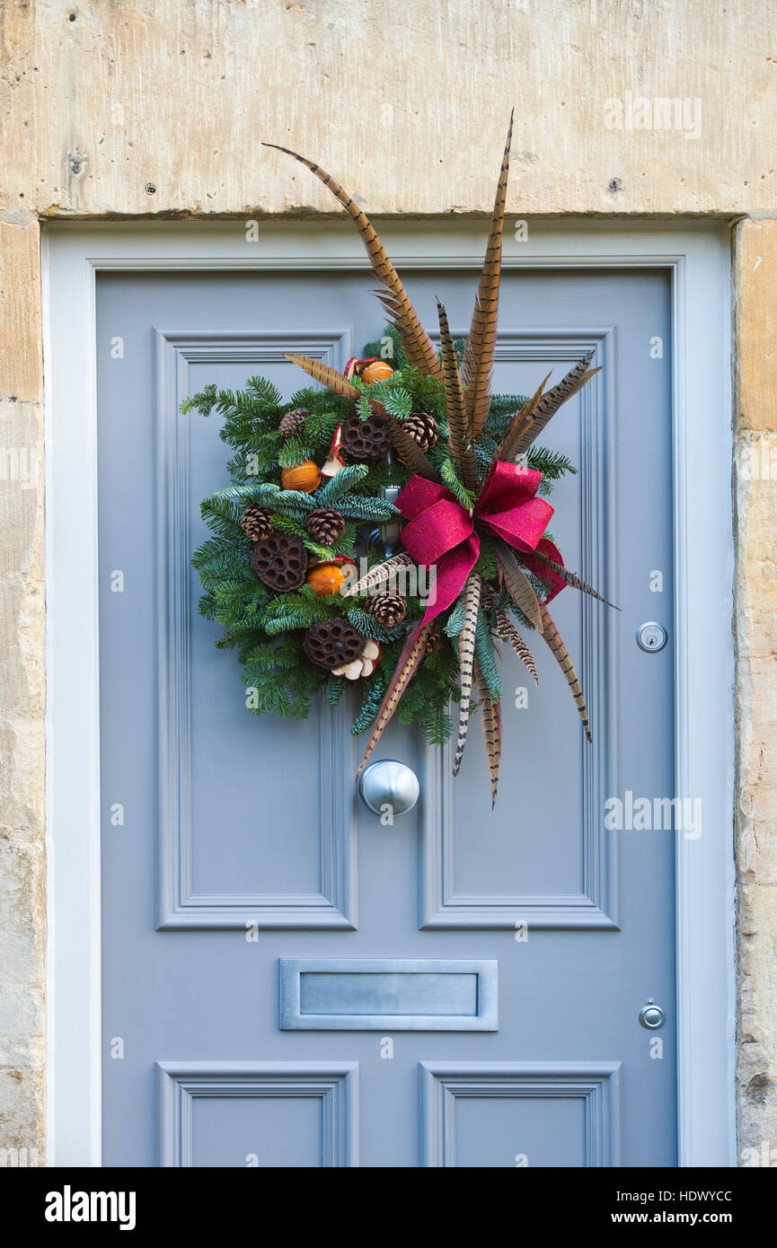 Christmas foliage, feather and fruit wreath on wooden door. Cotswolds, England Stock Photo