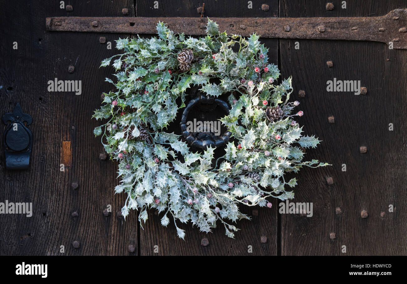 White Christmas holly wreath on old oak studded wooden door. Cotswolds, England Stock Photo