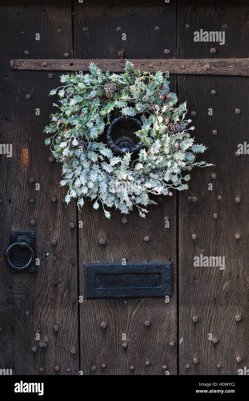 White Christmas holly wreath on old oak studded wooden door. Cotswolds, England Stock Photo