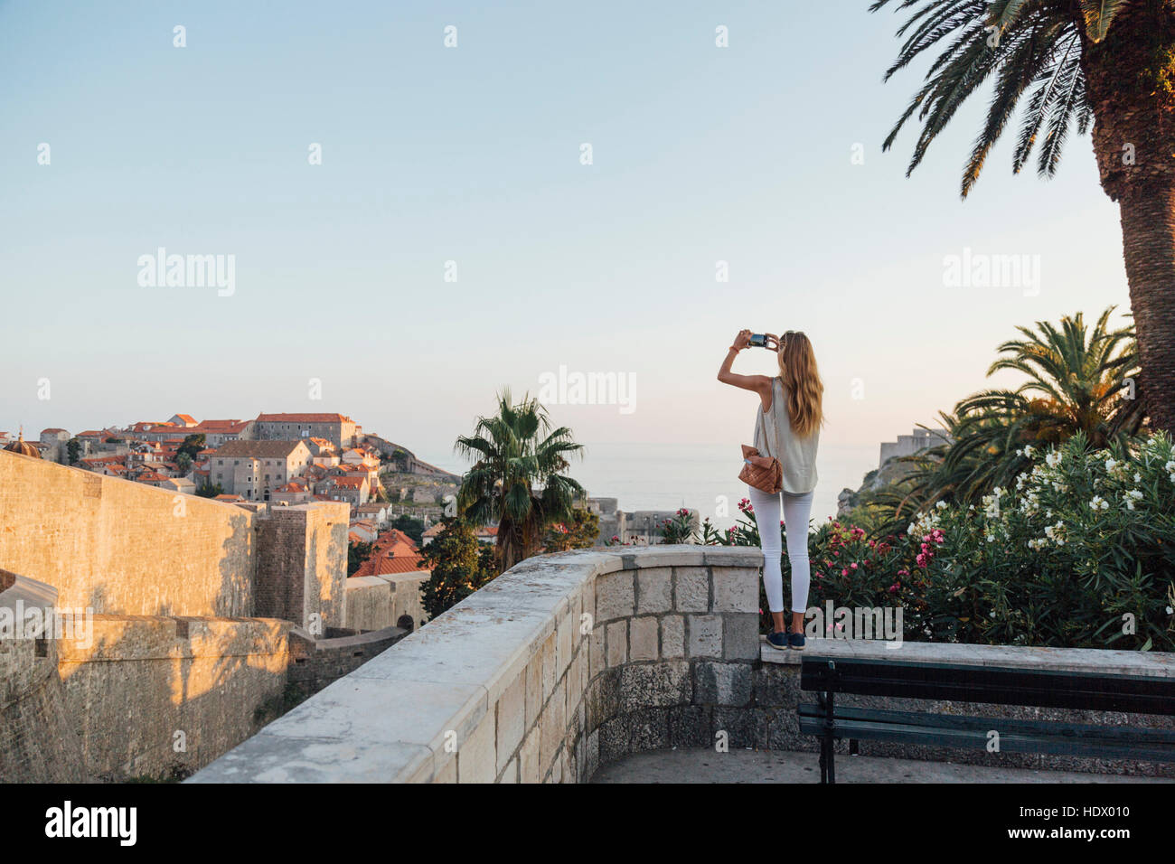 Caucasian woman standing on park wall photographing cityscape Stock Photo