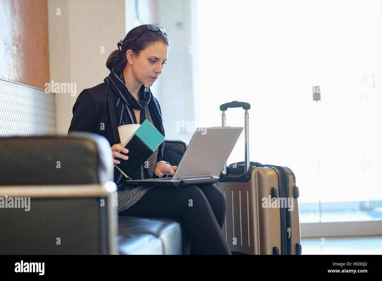 Hispanic woman holding passport using laptop in airport Stock Photo