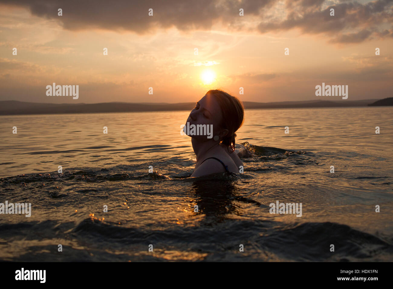 Caucasian woman swimming in lake at sunset Stock Photo