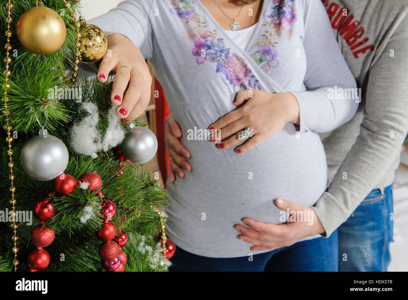 Pregnant Couple Near A Christmas Tree Husband Hugging His Pregnant Wife Girl Decorates A