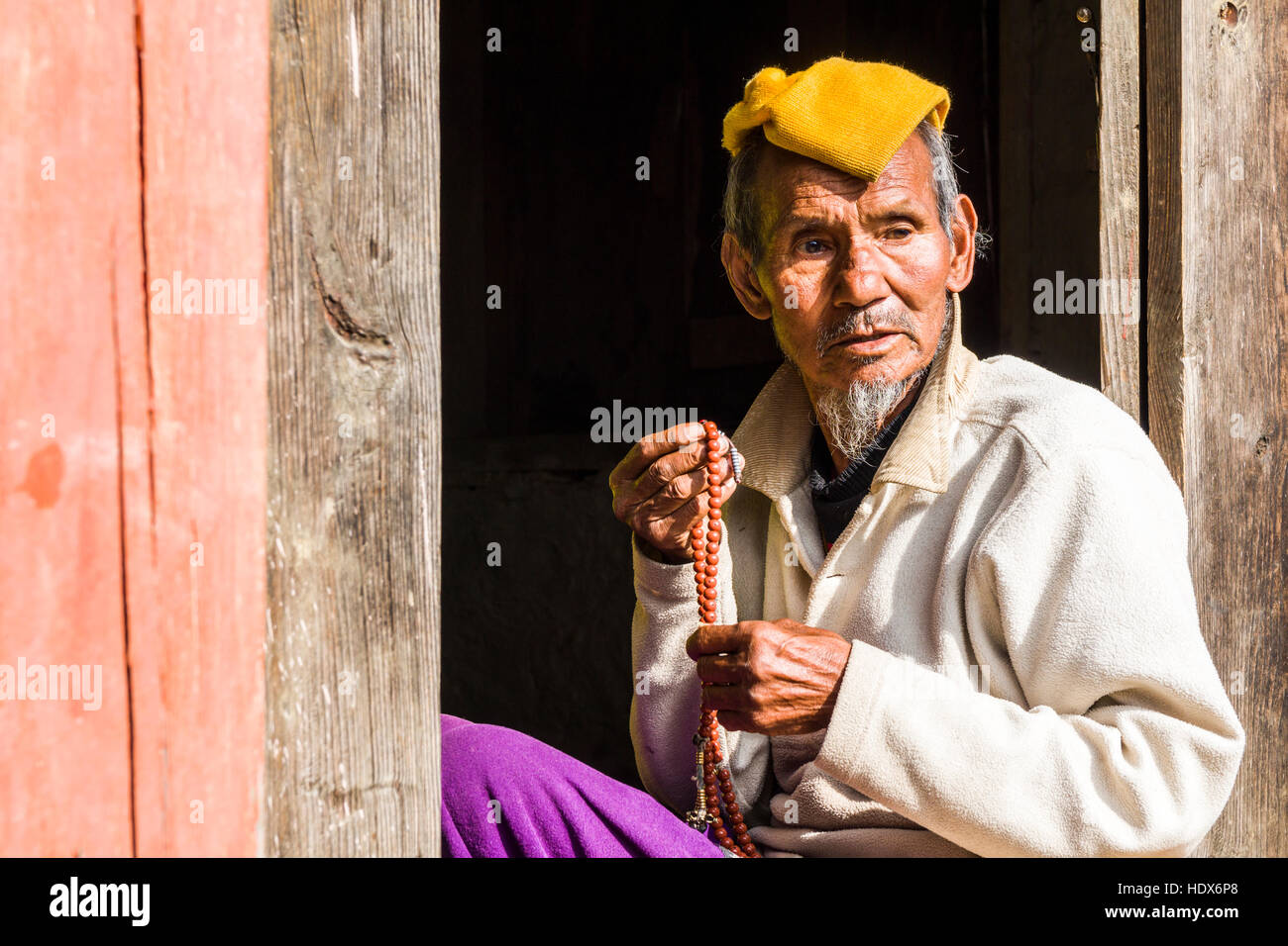 A man is sitting in a doorway and praying by using a mala Stock Photo