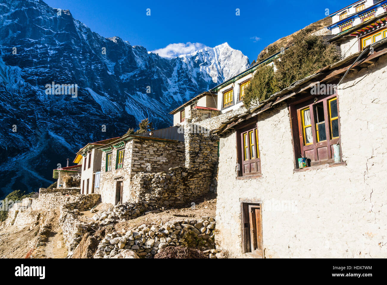 Buildings of the monastery Thame Gompa are located at a mountain slope, snow covered mountains in the distance Stock Photo