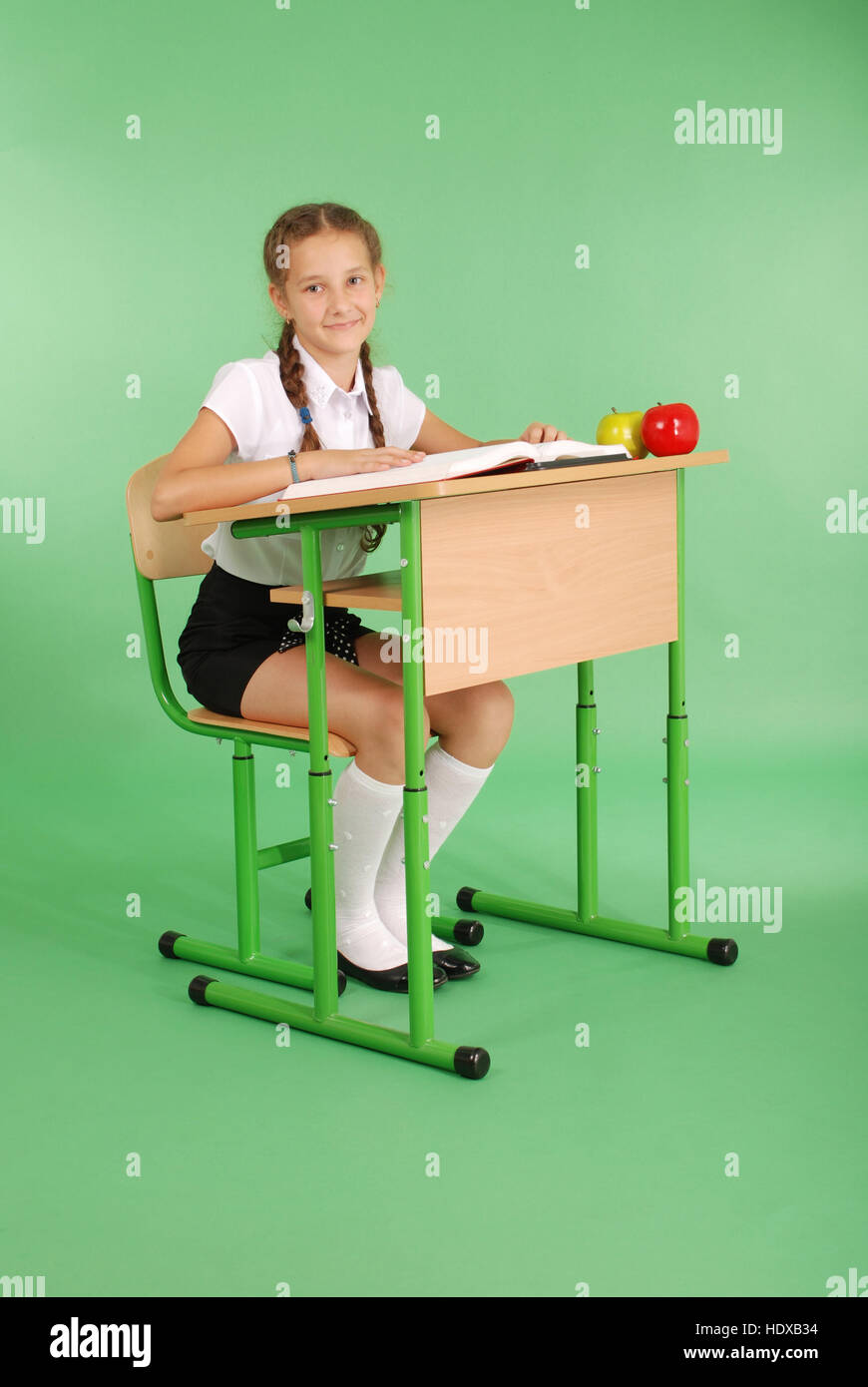 Girl in a school uniform sitting at a desk and reading a book isolated ...